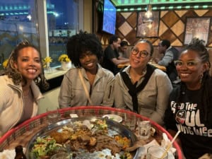 Three women sitting over a table with food, all smiling